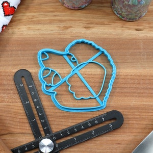 May include: A blue plastic cookie cutter shaped like a hedgehog. The cutter is on a wooden surface with a ruler and a rolling pin.