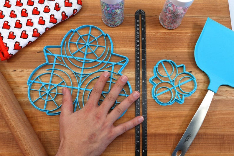 May include: A set of three blue plastic cookie cutters, one large circle with a web design, one smaller circle with a web design, and a three-circle flower design.