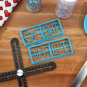 May include: Two blue plastic cookie cutters on a wooden surface. The cutters are shaped like the words "FIGHT" and "ACT".