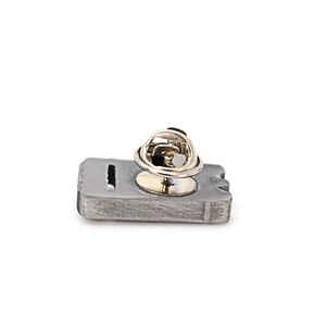 May include: A silver-toned metal pin shaped like a cassette tape with a silver-toned metal pin back.