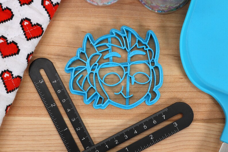 May include: A blue plastic cookie cutter shaped like a cartoon character with glasses and a smile.