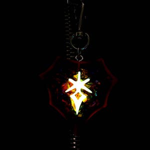 May include: A glowing white symbol in a red, iridescent, star-shaped pendant. The pendant is hanging from a silver chain.