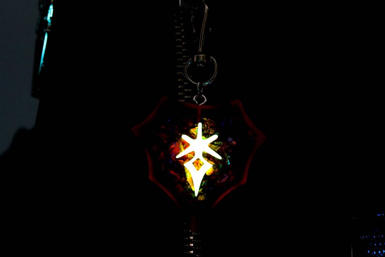 May include: A glowing white symbol in a red, iridescent, star-shaped pendant. The pendant is hanging from a silver chain.