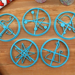 May include: Five blue plastic cookie cutters with different geometric designs. The cutters are on a wooden surface.