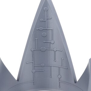 May include: A gray, 3D printed crown with a geometric design on the top. The crown is pointed and has a sharp, angular shape.