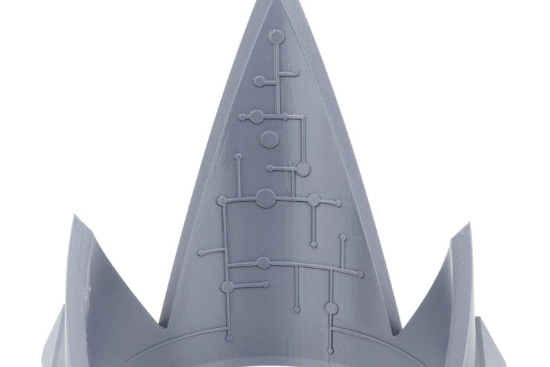 May include: A gray, 3D printed crown with a geometric design on the top. The crown is pointed and has a sharp, angular shape.