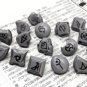 May include: A collection of 15 silver-colored metal dice with various symbols and designs. The dice are scattered on a white surface with Japanese text.