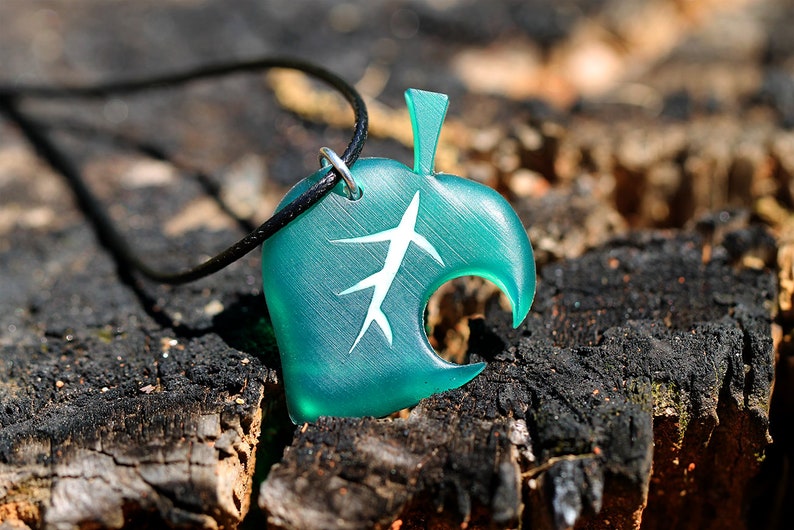 May include: A teal green leaf-shaped pendant necklace with a white leaf design. The necklace is made of resin and has a black cord.