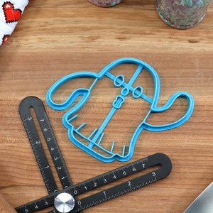 May include: A blue plastic cookie cutter shaped like a ghost with a face and a zipper down the front.