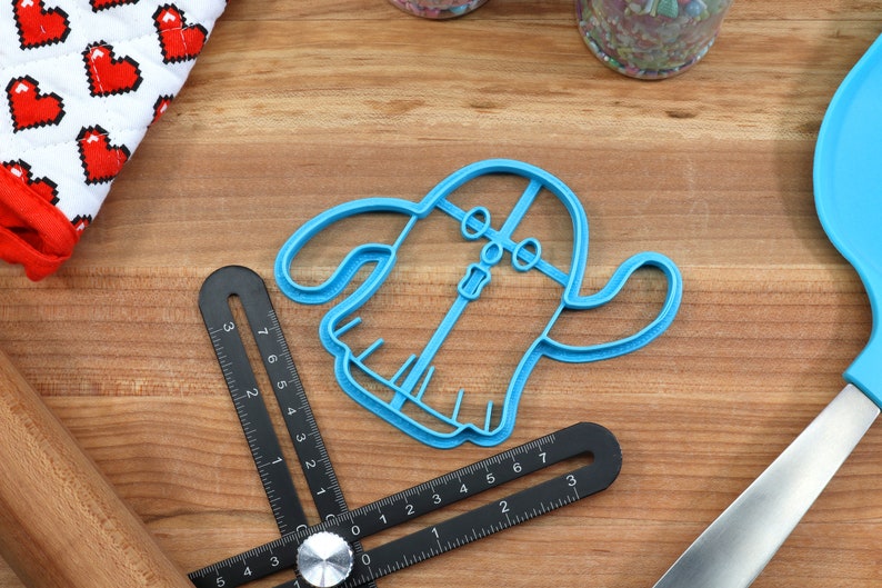 May include: A blue plastic cookie cutter shaped like a ghost with a face and a zipper down the front.