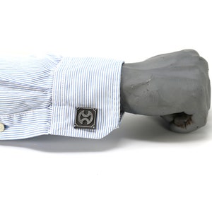 May include: A pair of silver cufflinks with a geometric design. The cufflinks are worn on a blue and white striped shirt cuff.