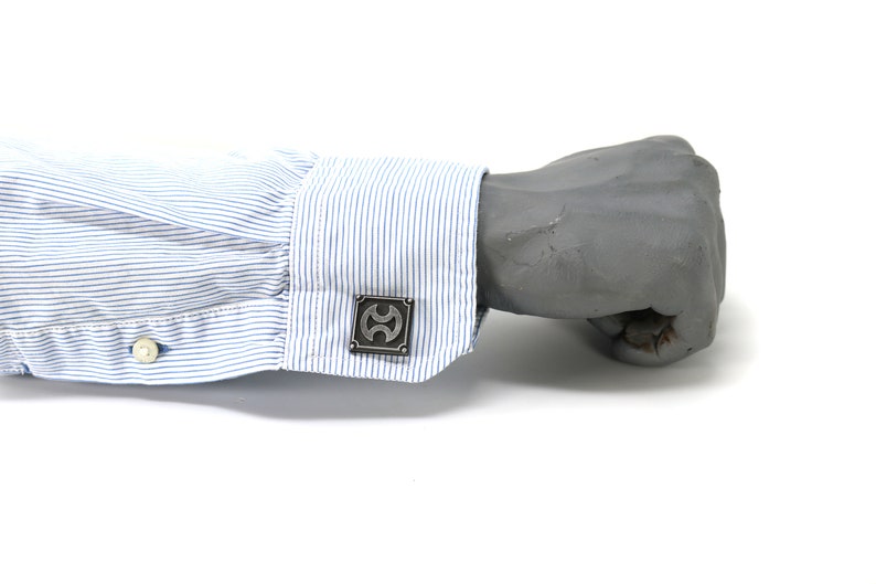 May include: A pair of silver cufflinks with a geometric design. The cufflinks are worn on a blue and white striped shirt cuff.