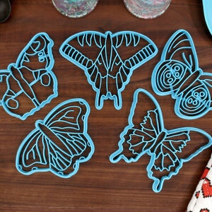 Puede incluir: Cinco cortadores de galletas con forma de mariposa azul sobre una superficie de madera.