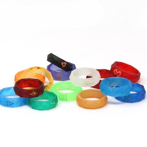 May include: A collection of colorful silicone rings with different symbols engraved on them. The rings are stacked and arranged on a white surface.