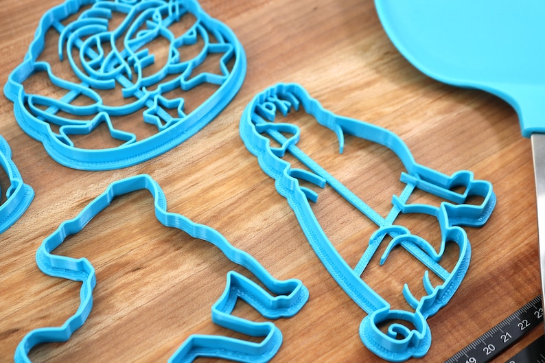 May include: A set of four blue plastic cookie cutters shaped like a person, a dog, a flower, and a star. The cutters are on a wooden surface.