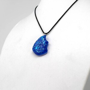 May include: A blue glass pendant with iridescent flecks hangs from a black cord necklace.