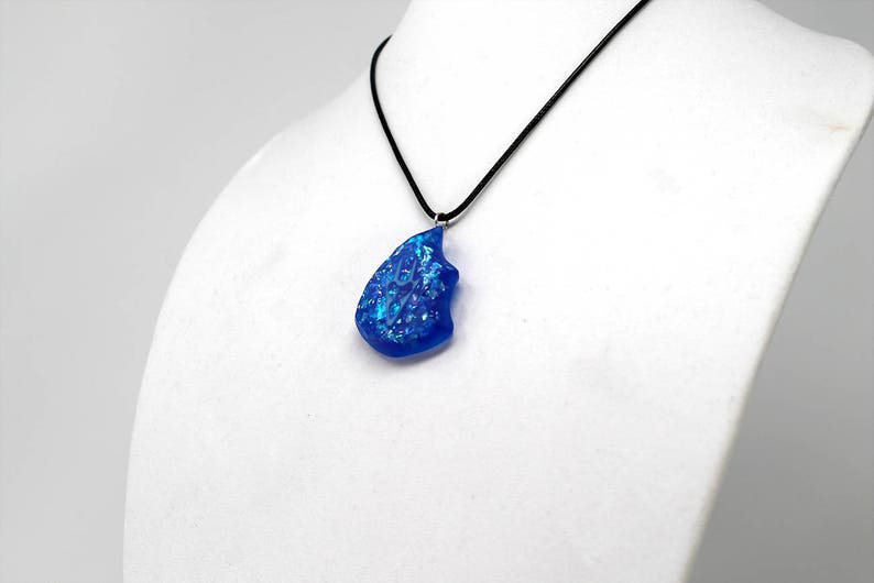 May include: A blue glass pendant with iridescent flecks hangs from a black cord necklace.