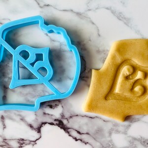 May include: A blue plastic cookie cutter shaped like the number "25" and a cookie dough cutout using the cutter.