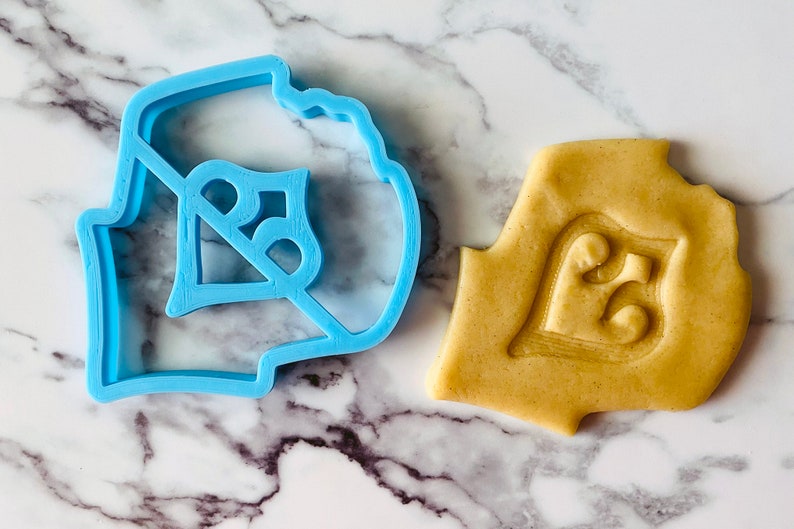 May include: A blue plastic cookie cutter shaped like the number "25" and a cookie dough cutout using the cutter.