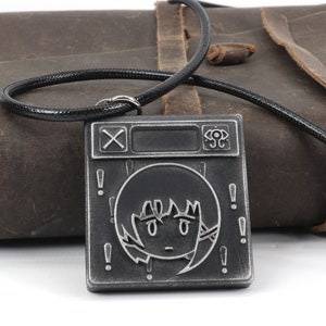 May include: A black and silver metal necklace with a square pendant featuring a stylized face with exclamation points around it. The pendant also has a cross and a circle with a dot in the center.