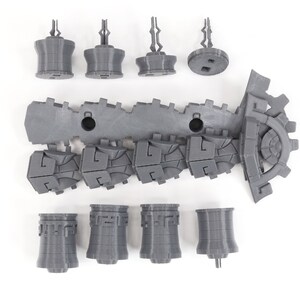 May include: A set of gray 3D printed plastic pieces for a model building kit. The pieces include a long, segmented track, a gear, and several towers.