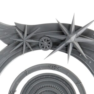 May include: A gray, stylized celestial archway with star and wing details. The design features multiple concentric arcs, with starburst and snowflake-like embellishments. The archway has a detailed, textured surface.