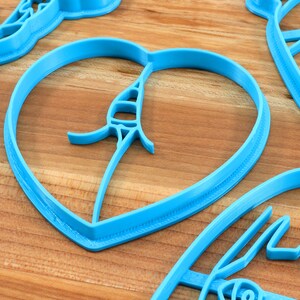 May include: A set of blue plastic cookie cutters in various shapes, including a heart, a leaf, and a flower. The cutters are on a wooden surface.