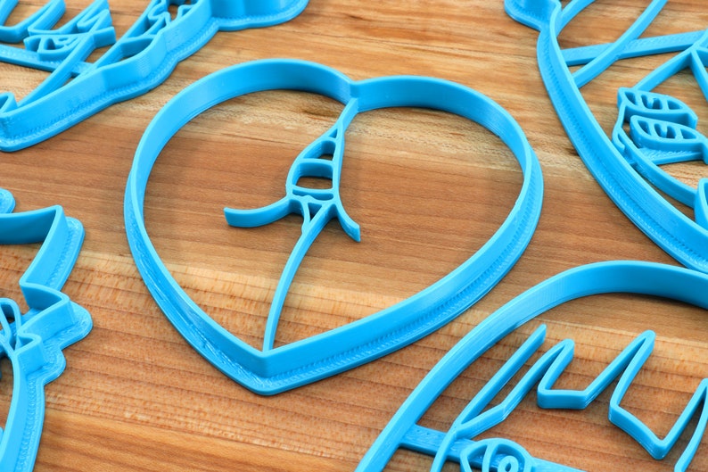 May include: A set of blue plastic cookie cutters in various shapes, including a heart, a leaf, and a flower. The cutters are on a wooden surface.