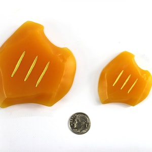 May include: Two orange, irregularly shaped, silicone objects with three gold lines on each. The objects are on a white surface.