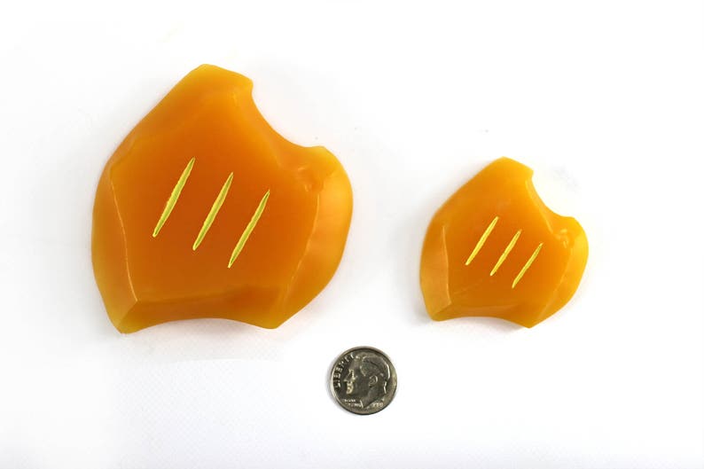 May include: Two orange, irregularly shaped, silicone objects with three gold lines on each. The objects are on a white surface.