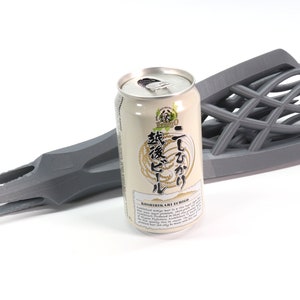 May include: A gray 3D printed object shaped like a hand holding a can of Japanese beer. The can is labeled "Echigo" and has Japanese text on it.