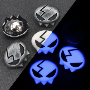 Peut inclure: Cinq boutons en forme de cr&acirc;ne avec un motif d'&eacute;clair. Les boutons sont argent&eacute;s avec des d&eacute;tails noirs et brillent en bleu dans le noir.