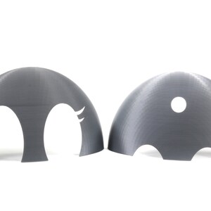 May include: Two gray plastic dome-shaped objects with cutouts. One dome has two eye-shaped cutouts with eyelashes. The other dome has a single round cutout.