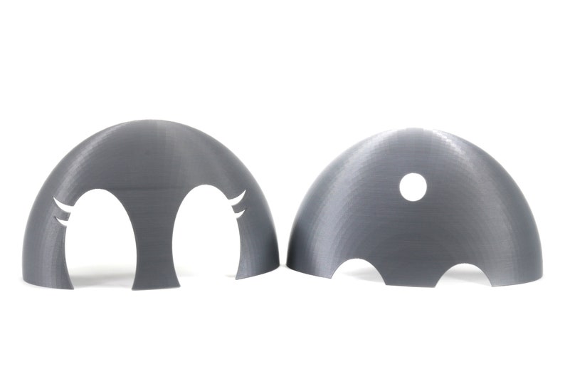 May include: Two gray plastic dome-shaped objects with cutouts. One dome has two eye-shaped cutouts with eyelashes. The other dome has a single round cutout.
