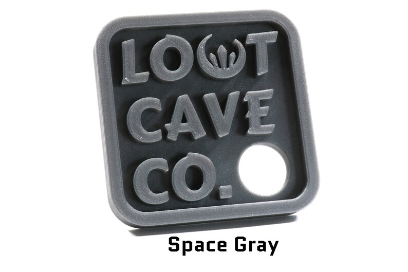 May include: A gray plastic key chain with the text "LOOT CAVE CO." and a small hole in the center. The key chain is a square shape with rounded corners.
