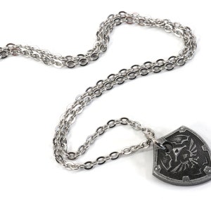 May include: A silver chain necklace with a silver pendant shaped like a shield with a black and white design.