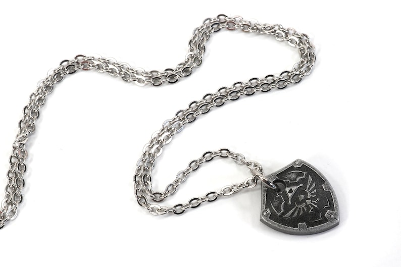 May include: A silver chain necklace with a silver pendant shaped like a shield with a black and white design.