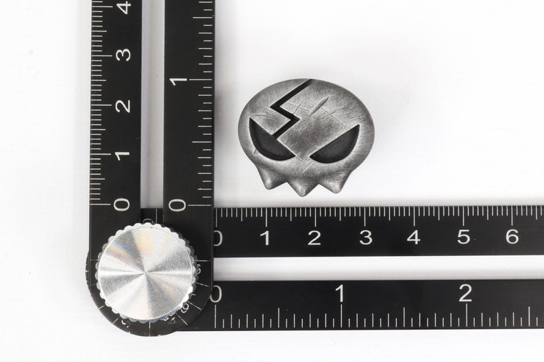 Peut inclure: Un charme en forme de cr&acirc;ne argent&eacute; avec un motif d'&eacute;clair et une surface textur&eacute;e. Le charme mesure environ 2,5 cm de diam&egrave;tre.