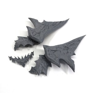 May include: Four grey 3D printed pieces that resemble a dragon's wings. The pieces are broken into smaller parts.