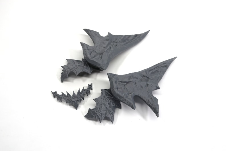 May include: Four grey 3D printed pieces that resemble a dragon's wings. The pieces are broken into smaller parts.
