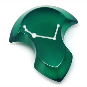 Op de afbeelding: Een unieke, smaragdgroene klok met een witte, gestileerde wijzerplaat. De klok heeft een gladde, gebogen vorm en een glanzende afwerking. Het ontwerp is modern en abstract, geschikt voor interieurdecoratie.