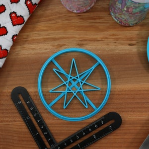 May include: A blue plastic cookie cutter shaped like a star with eight points. The cutter is on a wooden surface with a ruler and a blue silicone spatula.
