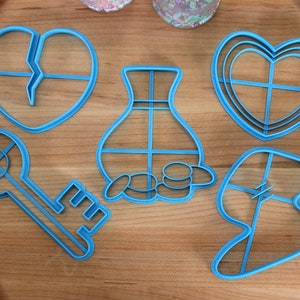 May include: A set of six blue plastic cookie cutters shaped like a key, a vase, a broken heart, a whole heart, a money bag, and a lightning bolt.
