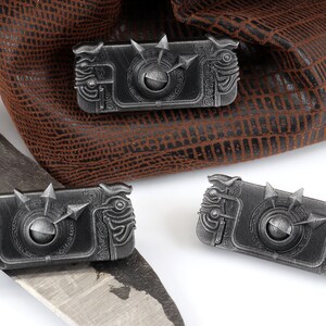 May include: Three silver metal dice with intricate designs and a spinning wheel in the centre. The dice are on a white surface.