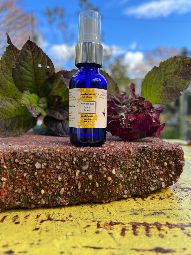 May include: A blue glass bottle with a silver pump top. The bottle is labeled "Honeybee Venom Oil Infusion" and "From the Bees Rejuve Serum". The label also says "Gentle Wrinkle Reduction" and "1 fl oz / 30 ml".