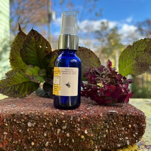 May include: A blue glass bottle with a silver cap and a white spray nozzle. The bottle is labeled with the text "Produced by: NewApiapis.etsy.com  Montclair, NJ 07043". A small bee illustration is on the label.