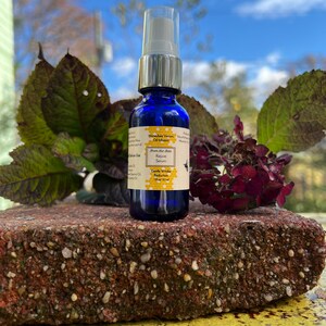 May include: A small blue glass bottle with a white spray top. The bottle is labeled "Honeybee Venom Oil Infusion" and "Gentle Wrinkle Reduction". The bottle is sitting on a red brick.