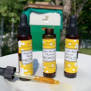 May include: Three small brown glass bottles with droppers, each containing a clear liquid. The bottles are labeled "From the Bees Natural Propolis" and "Spagyric Ethyl Alcohol Tincture". The bottles are sitting on a white plate.