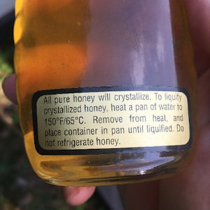 May include: A glass jar of honey with a black label that reads: "All pure honey will crystallize. To liquify crystallized honey, heat a pan of water to 150&deg;F/65&deg;C. Remove from heat, and place container in pan until liquified. Do not refrigerate honey."