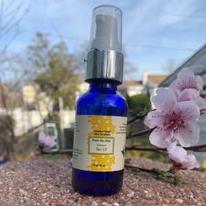 May include: A blue glass bottle with a silver pump top and a white label. The label says "Honeybee Venom Olive Oil Infusion From the Bees Venom Skin Oil 1 fl oz / 30 ml".
